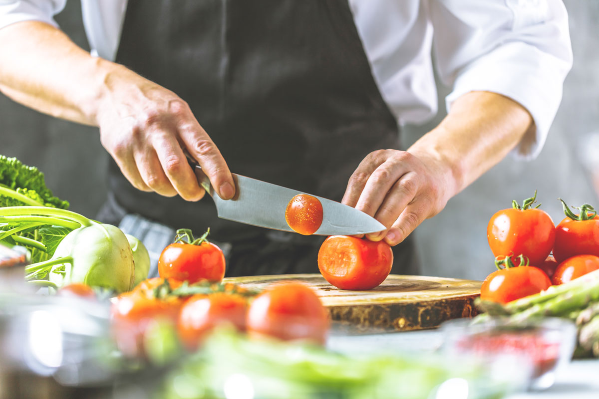 Ein Mann schneidet Tomaten mit einem Küchenmesser aus einem Messerblock