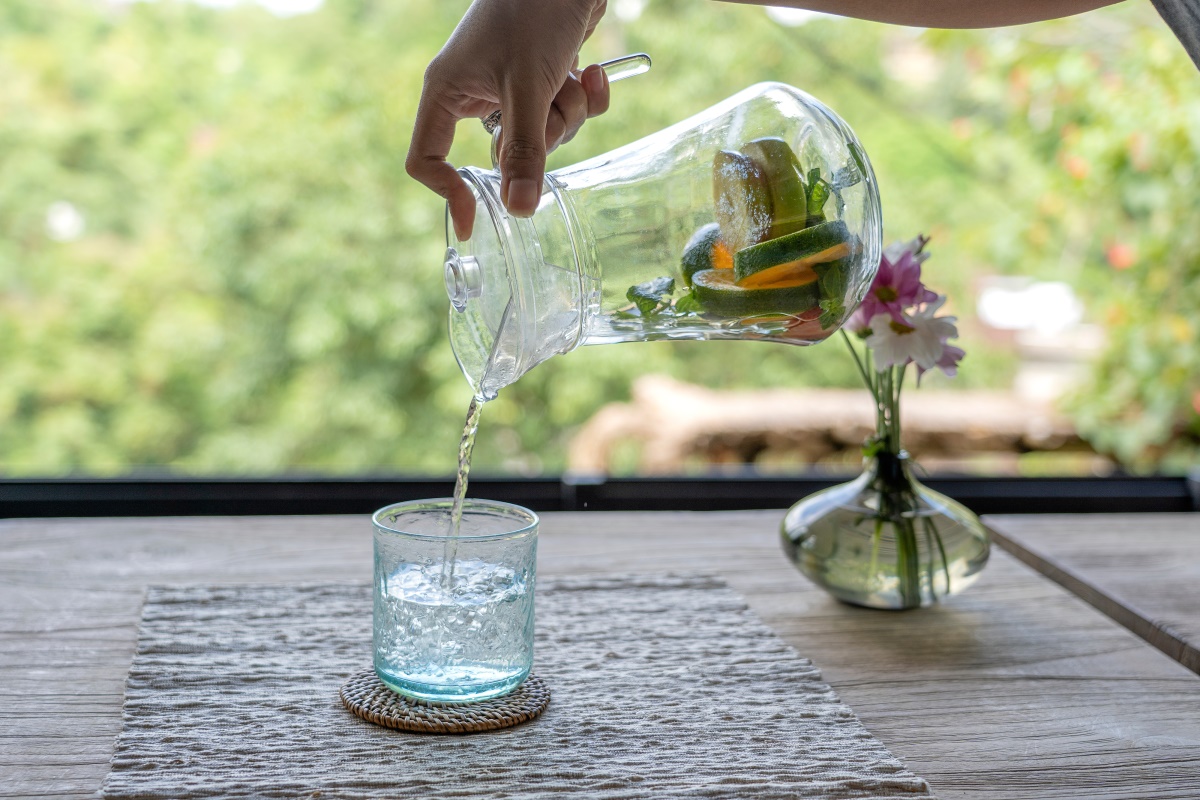 Eine schlanke Hand gießt Wasser aus einer Karaffe in ein Glas